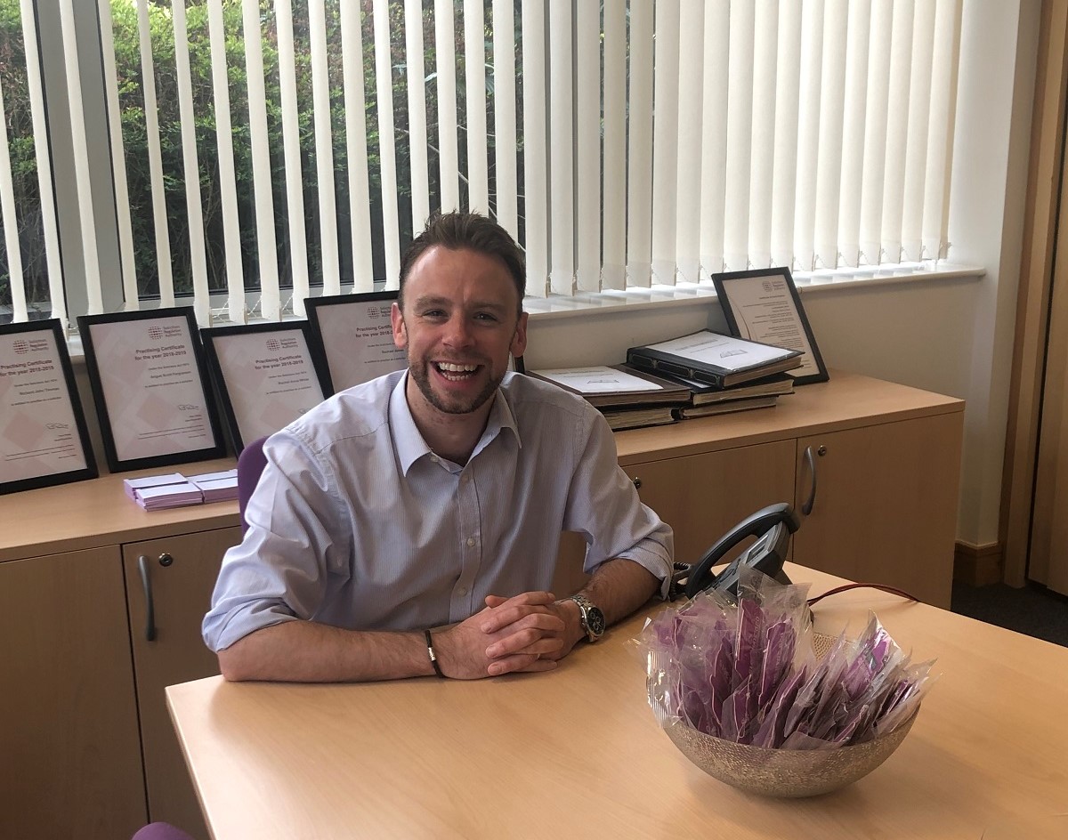 persoanl injury solicitor Andrew Last of mooneerams of Cardiff in white shirt sitting at long table with in front of window