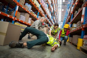 Man being helped by colleagues following an injury from a slip trip or fall in a warehouse