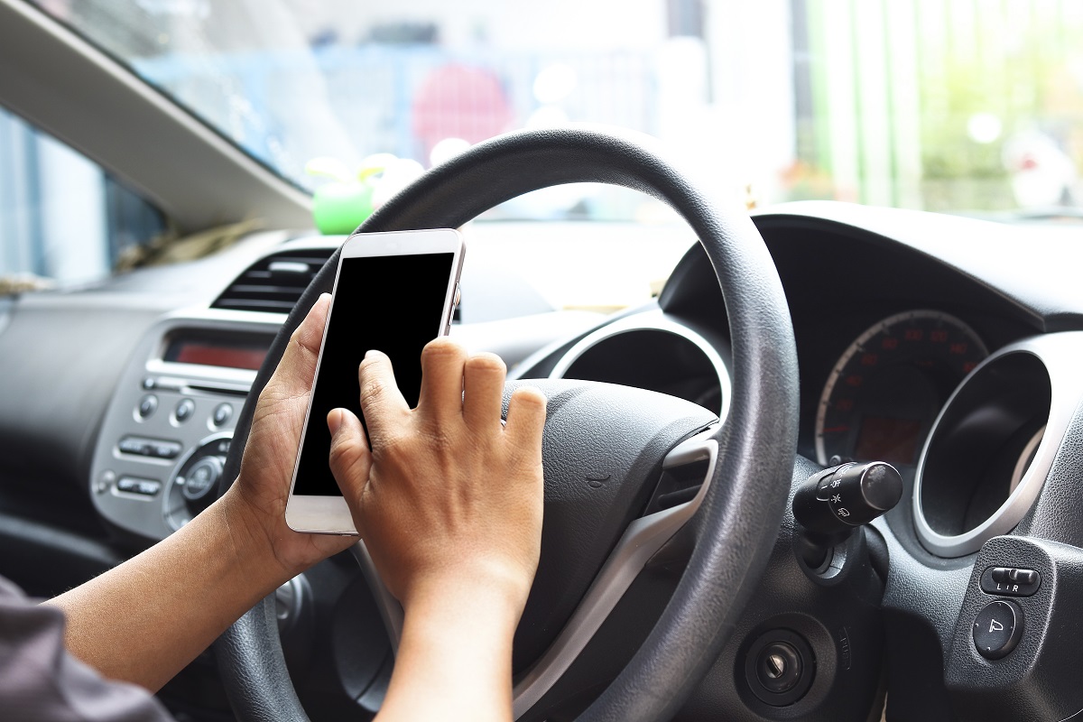 man driving car with one hand and holding phone in the other