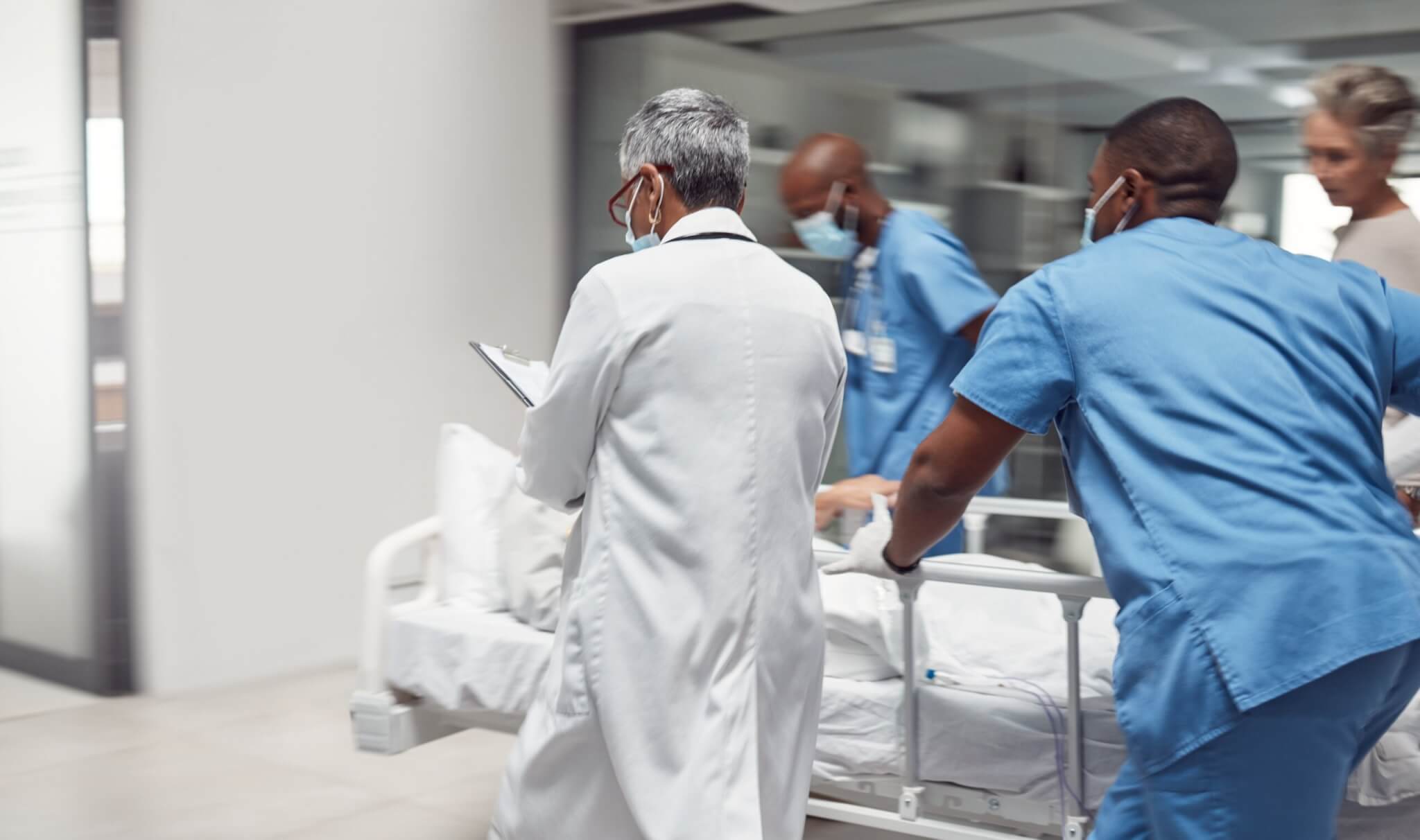 Medical professionals pushing a gurney through hospital corridor.